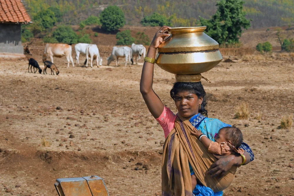 Woman holding baby with water jug on her head
