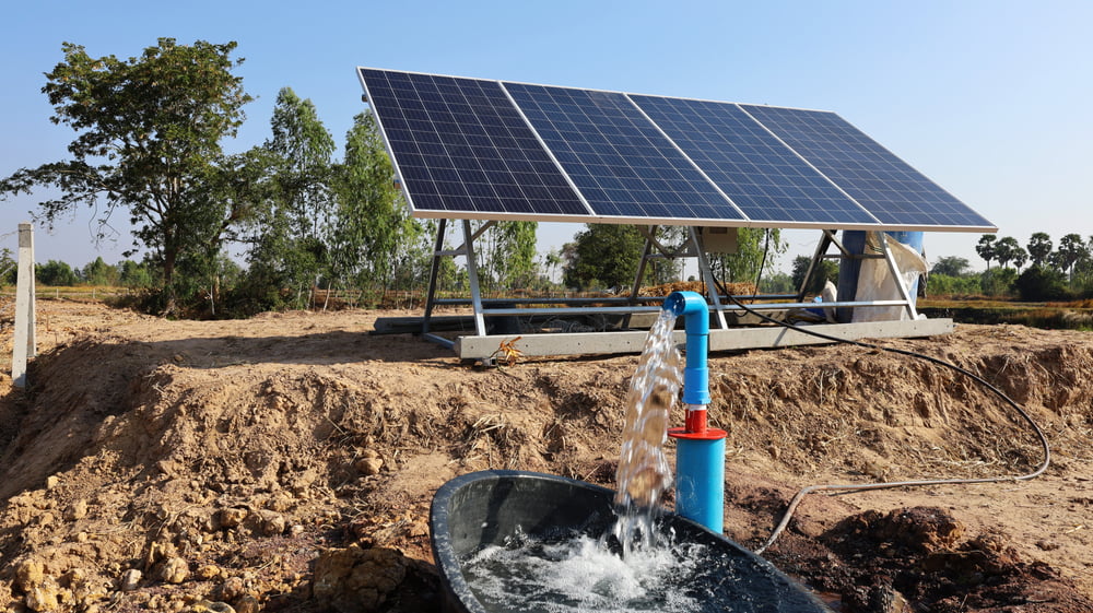 ground water pump pushing water out into a black bucket, powered by solar panel located behind it
